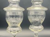 two clear glass vases with lids on a black surface