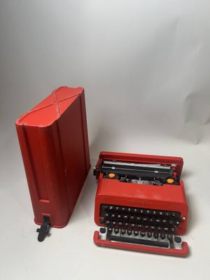 une machine à écrire rouge à côté d'une boîte rouge posée sur une surface blanche