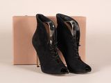 des bottines noires en daim à lacets, posées devant une boîte en carton