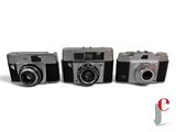 three old cameras are lined up in a row on a white surface