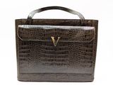 a close up of a brown crocodile skin handbag with a gold v on the handle