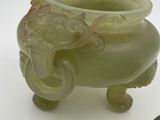 a green vase with an elephant head on it next to a green hat