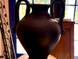 un vase noir posé sur une table en bois devant une fenêtre