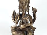 brass statue of ganesh sitting on a rock with two hands raised