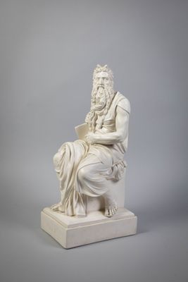 une statue blanche représentant un homme assis sur une chaise, un livre à la main