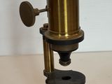 Un vieux microscope est posé sur une table en bois.