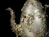 a silver vase with a bird on it on a black background
