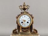 une horloge dorée et blanche posée sur un socle, surmontée d'une couronne