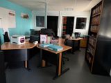 a room with a desk, chair, bookshelf, and a refrigerator in it