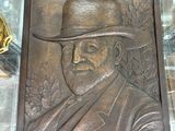 une plaque en bronze représentant un homme coiffé d'un chapeau, posée sur une table en verre