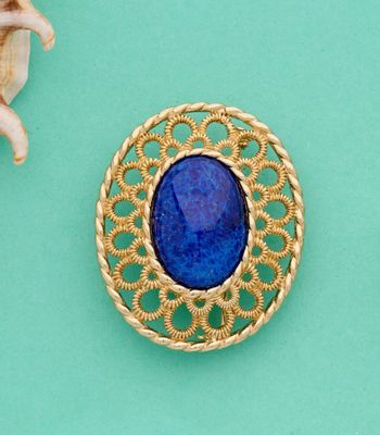 broche plaquée or ornée d'une pierre bleue entourée de coquillages sur fond turquoise