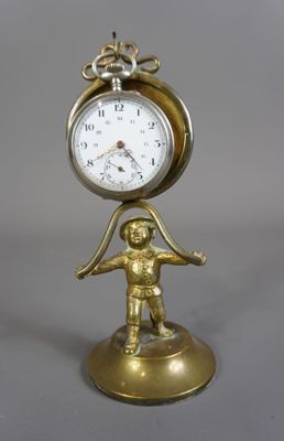 une horloge en or posée sur un socle, sur lequel se trouve un petit garçon