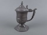 une cafetière ancienne en métal argenté, surmontée d'un oiseau