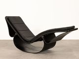a black leather lounge chair with a curved back and foot rest