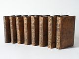 six old books are lined up in a row on a white surface