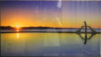tableau représentant un coucher de soleil sur un plan d'eau, avec une jetée au premier plan