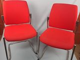pair of red office chairs with chrome legs and arms