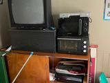 une télévision et un micro-ondes dans une pièce où le sol est encombré d'objets