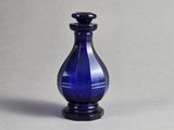 un vase en verre bleu avec un socle noir posé sur une surface grise