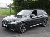 the bmw x3 is parked in a parking lot near a fence