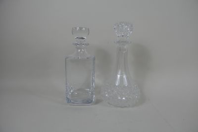 Deux carafes en verre. Une à section carrée avec bouchon et …