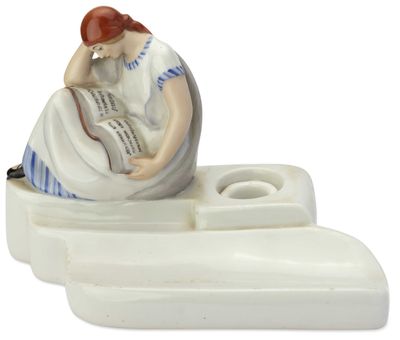 une figurine représentant une femme en train de lire un livre sur un bateau