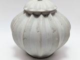 un vase blanc muni d'un couvercle, posé sur une surface blanche