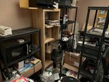 a messy room with a fan, bookshelf, desk, and other clutter