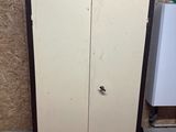 une armoire haute placée dans un coin de la pièce, à côté d'un réfrigérateur