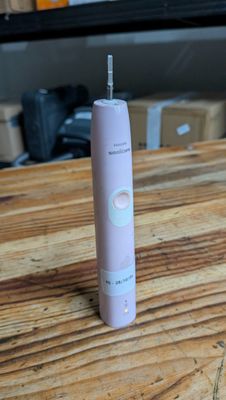 une brosse à dents électrique rose posée sur une table en bois