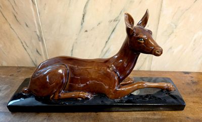 statue d'un cerf couché sur un socle noir posé sur une table en bois