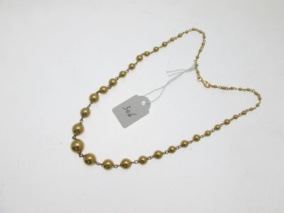 un gros plan d'un collier de perles dorées posé sur une surface blanche