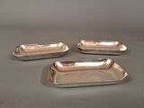 three silver plated trays with handles on a gray surface