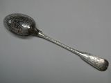silver plated spoon with a pattern on it on a gray surface