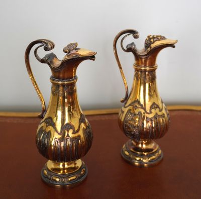 deux vases en or posés sur une table, avec un mur blanc en arrière-plan