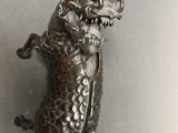 a silver statue of a cat with a bell hanging from it ' s back