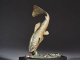 une sculpture représentant un poisson posée sur un socle en bois, avec un fond noir
