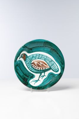 assiette en verre vert sur laquelle est représenté un oiseau, posée sur une surface blanche