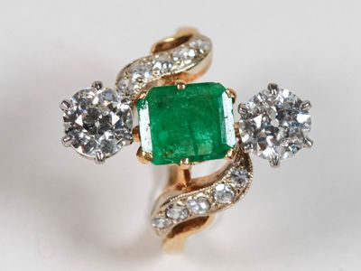 un gros plan d'une bague sertie d'une émeraude et de diamants sur une surface blanche