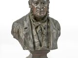 statue représentant le buste d'un homme en costume-cravate, posée sur un socle en bois
