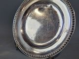 un plat ancien en argent aux bords perlés posé sur une table