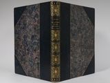 an old black book with gold trim sitting on top of a white table