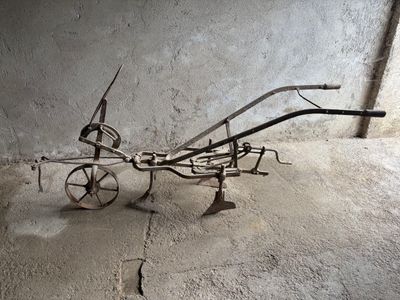 une charrue métallique tirée par des chevaux, posée dans une pièce en béton