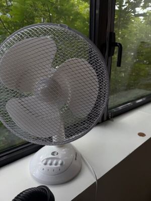 un ventilateur posé sur le rebord d'une fenêtre, devant celle-ci