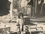 une photo en noir et blanc d'une petite fille debout devant une cabane