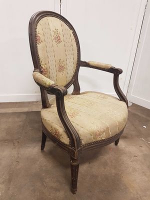 une chaise à l'ancienne, dont le dossier et les accoudoirs sont recouverts d'un tissu à motifs floraux
