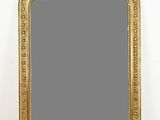 un miroir au cadre doré ouvragé posé sur un parquet, près d'un mur blanc