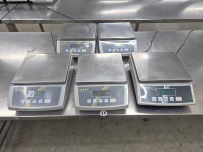 Quatre balances électroniques sont posées sur une table dans un entrepôt