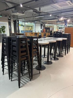 Des tables et des chaises sont alignées dans une grande pièce dotée de nombreuses fenêtres.