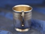 a silver cup with a gold handle on a blue cloth